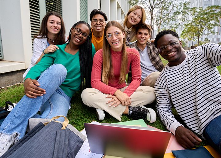 Group of students sitting together on the grass with a laptop and notebooks